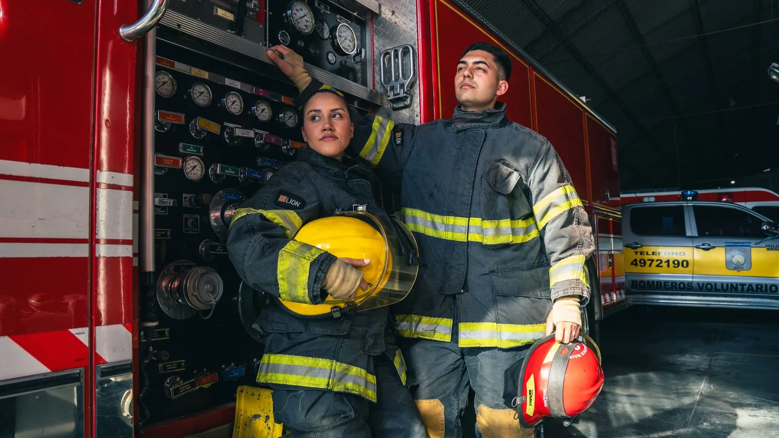 Firefighters in turnout gear beside a fire engine in the station bay