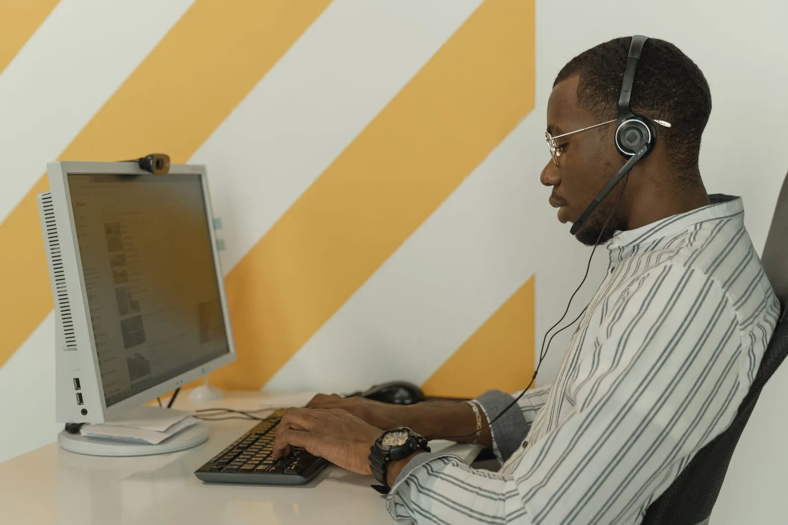 Office worker with a headset typing at a desktop computer